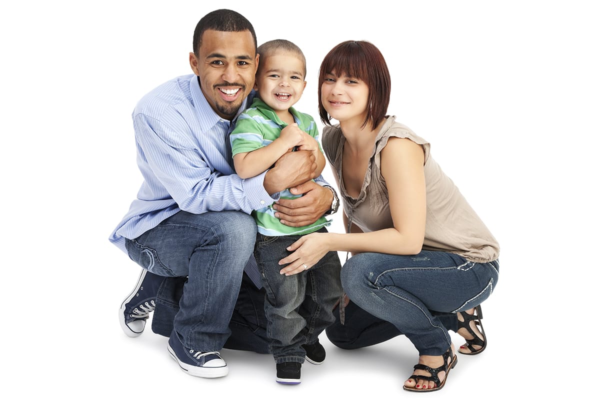 Young parents kneeling on ground with son smiling for the camera against a white background